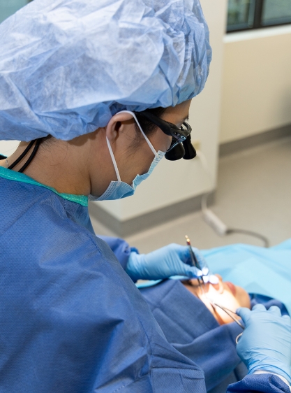 Dr. Kim, fully dressed in surgical gear, performing a facial plastic surgery procedure.